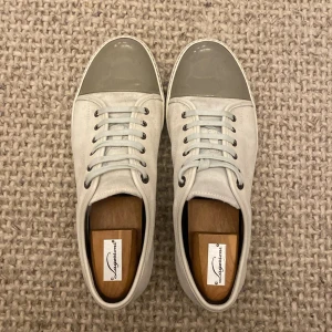 Lanvin cap toe - Snygga sneakers från Lanvin i ljusbeige mocka med grå lackad rund tå. Skorna har vita snören och metallfärgade öljetter, samt en platt sula i matchande ton. Perfekt för dig som gillar stilrena och exklusiva detaljer. Mockan är en blandning mellan vit och beige väldigt snygg! Fråga på så mycket som helst!