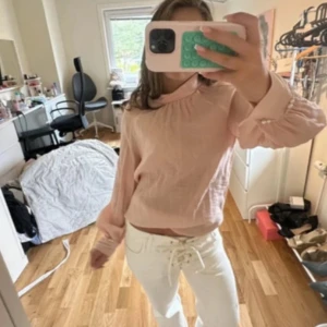 Ljusrosa blus med puffärm och pärlknappar - Supersöt ljusrosa blus med puffiga långärmar och fina pärlknappar vid ärmsluten. Blusen har en hög krage med rynkdetaljer och är gjord i ett tunt, luftigt tyg som känns riktigt fräscht.