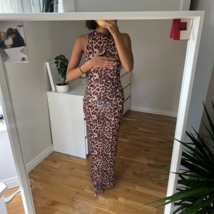 Leopardmönstrad långklänning - Älskar denna! Perfekt över bikini eller på fest på kvällen! En snygg leopardmönstrad långklänning med ärmlös design och rund hals. Klänningen är figurnära och har en beige och brun färgskala. Materialet känns lätt och stretchigt, perfekt för dig som vill sticka ut med ett djuriskt mönster.
