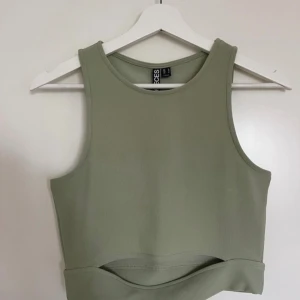 Grön croppad träningstopp från Pieces - En croppad linnetopp från Pieces till träning i en ljusgrön ton. Modellen är ärmlös med rund hals och har en cutout-detalj nedtill framtill. Perfekt för dig som gillar lite enklare plagg till träning eller vardags. Materialet är mjukt och stretchigt syntet för skön passform.