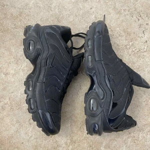 Nike Air Max Plus helsvarta sneakers - Säljer ett par helsvarta Nike Air Max Plus med ikonisk vågig design och synliga luftbubblor i sulan. Skorna har mesh- och syntetöverdel, svarta detaljer och snörning. Perfekta för dig som gillar chunky sneakers med streetkänsla.