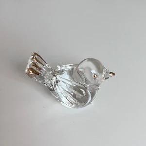 Glasfågel med gulddetaljer - Unik liten fågel i transparent glas med skimrande gulddetaljer på näbb, öga och stjärt. Kommer i en vit presentask med satinliknande tyg. Perfekt accessoar för dig som gillar söta och stilrena smycken. Aldrig använd. Önskar du veta mer? Tveka inte att höra av dig!