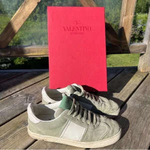 Valentino Garavani sneakers i mocka - Snygga sneakers från Valentino Garavani med box i ljusgrön mocka med vita detaljer och snörning. Skorna har en klassisk låg siluett och en vit platt sula med svart mönstrad undersida. Perfekta för dig som gillar exklusiva och stilrena sneakers.