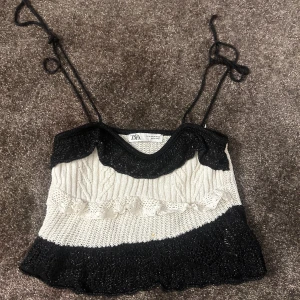 Stickad svartvit linnetopp från Zara - Säljer en stickad linnetopp från Zara i svart och vitt med smala axelband som knyts. Toppen har en snygg volangdetalj framtill och är croppad med kontrast mellan svart och vit stickning. Perfekt för dig som gillar unika detaljer och cool stil.