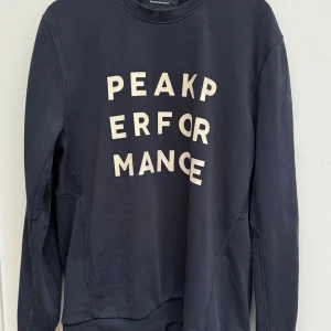 Mörkblå Peak Performance sweatshirt - Snygg mörkblå sweatshirt från Peak Performance med vit text på framsidan. Tröjan har rund hals, ribbade muddar och lång ärm. Perfekt för dig som gillar stilren design och vill ha en bekväm tröja i bomull.