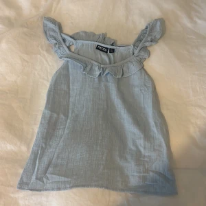 Ljusblå linnetopp med volang - ljusblå linnetopp med volangdetaljer längs axelbanden och halsringningen