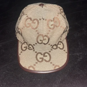 Gucci keps  - Säljer en snygg keps från Gucci i beige och brunt med det klassiska GG-monogrammet över hela kepsen. Kepsen har böjd skärm med brun kant och är tillverkad i bomullsmix. Perfekt för dig som vill sticka ut med en lyxig accessoar.