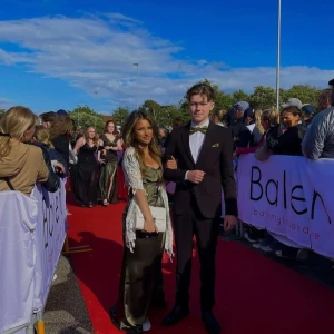 Olivgrön balklänning - Säljer en elegant olivgrön långklänning med omlott och djup v-ringning. Klänningen har kort ärm och ett glansigt material som ger en lyxig känsla. Perfekt för balen