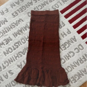 Brun långkjol med volang från Gina Tricot - Säljer en brun långkjol från Gina Tricot i storlek 32. Kjolen har smockad midja och hela kjolen är smockad med en bred volang längst ner. Materialet är mjukt och lätt, perfekt för dig som gillar boho-vibe och vill ha något bekvämt men ändå snyggt.