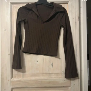 Brun ribbad långärmad tröja - Säljer en brun långärmad tröja med ribbad struktur och v-ringad krage. Tröjan har en snygg, figurnära passform och är perfekt för lager-på-lager. Enkel att matcha med både jeans och kjol.