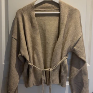 Beige stickad kofta med knytband - Mysig o superfin stickad kofta. Koftan har ett knytband i midjan som ger en snygg omlott-look, man kan ta bort snöret om man vill!🩷🩷Den är även nytvättad!!