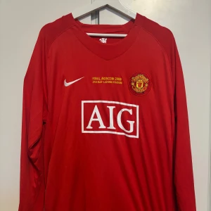 Manchester United Final Moscow 2008 Ronaldo - Legendarsk Manchester United fotbollströja från Champions League-finalen i Moskva 2008 med Ronaldo 7 på ryggen. Röd långärmad modell med AIG som sponsor, klubbmärke på bröstet och silvriga detaljer. Perfekt för samlare eller fans av klassiska tröjor.