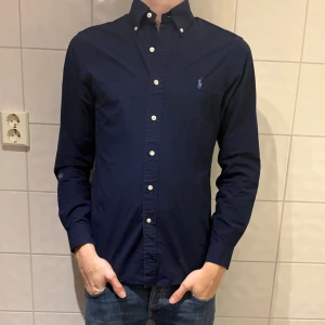 Mörkblå skjorta från Ralph Lauren - Klassisk mörkblå skjorta från Ralph Lauren, i jätte bra skick! Jag på bilden är 184cm lång och väger 70kg. Hör av er vid frågor eller funderingar!👌🤩