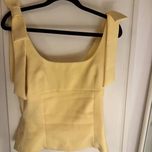Gul linnetopp med rosett från Zara - Supersöt ljusgul linnetopp från Zara med breda axelband och fina rosettdetaljer på axlarna. Passar xs-s, säljer då den är för liten för mig!