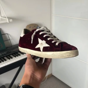 Vinröda Golden Goose sneakers Limited edition - Säljer ett par snygga Golden Goose sneakers i vinröd sammet. Dessa är asfeta och dessutom ÄKTA✨ då de är utrustade med NFC authentification (bild 3). Riktigt bra skick på dessa! Den enda defekten är några små slitningar (bild 5) på tyget, men är ingenting som märks av vid användning. Köpta i storlek 41 men psssar utan problem 40. Dustbag och box följer med vid köp, bara inte toppskick på boxen. 