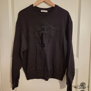 Svart sweatshirt Tiger of Sweden Jeans - Svart sweatshirt från Tiger of Sweden Jeans i storlek M. Tröjan har ett broderat emblem framtill och klassisk rund hals. Materialet är mjuk bomull och passformen är normal med långa ärmar. Perfekt för dig som gillar stilrena och coola detaljer.