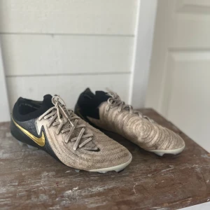 Nike phantom Gx 2 elite FG - Säljer ett par Nike fotbollsskor då dom inte används längre. Dom är i väldigt bra skick faktiskt men det ända är att dom kanske ser lite smutsiga ut vilket dom lite granna är (ser dock bättre ut i verkligheten). Jag har tvättat så gott det går men själva delen där det är smutsigt är extremt svår att göra ren så förr eller senare hade de skett ändå. Dom är elite och fg storlek 41!