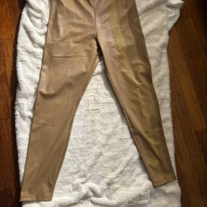 Beiga skinnleggings. stl L - Snygga beiga leggings i skinnimitation från cubus. De har en tight passform och hög midja, vilket ger en clean och modern look. Perfekta att styla med oversized tröjor eller crop tops. Materialet är mjukt och följsamt för extra komfort.