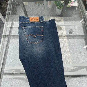 Replay M909 Regular Fit Jeans – W34 L36 – Mörkblå Denim - Snygga och tidlösa jeans från Replay, modell M909.036. Tillverkade av 100 % bomull för den klassiska denimkänslan – hållbara, mjuka och med perfekt fall. Mörkblå tvätt med lätt slitningar som ger en autentisk vintage-look. Rak passform (regular fit) som sitter bekvämt och passar de flesta kroppstyper.  📏 Storlek: W34 L36 🌍 Tillverkade i Tunisien 🧵 Kvalitetsdenim från Replay Blue Jeans-serien 🧼 I mycket bra skick – inga fläckar eller större slitage  Perfekta för dig som gillar casual premiumstil 