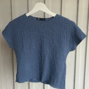 Blå strukturerad topp från Zara - Säljer en blå topp från Zara med korta ärmar och en cool, strukturerad yta. Toppen har en rak passform. Jättefin!!