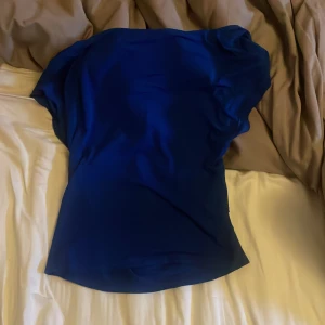 Mörkblå axelbandslös tubtopp - Säljer en stilren mörkblå tubtopp i mjukt och stretchigt material. Toppen är axelbandslös och har en enkel, slät design som sitter snyggt mot kroppen. Perfekt för dig som gillar minimalistisk stil och vill ha en topp som sticker ut med sin djupa blå färg.