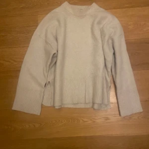 Beige stickad tröja från Bershka - Mysig beige stickad tröja från Bershka i storlek XS. Tröjan har lång ärm, ribbad kant nedtill och vid ärmslut samt en liten slits på sidan.