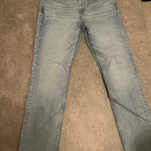 Ljusblå slim jeans från H&M - Säljer ett par ljusblå slim fit jeans från H&M med klassisk femficksdesign och knappstängning. Jeansen har raka ben och är tillverkade i mjukt denimtyg med snygga slitningar och detaljer i kopparfärgad metall. Perfekt för dig som gillar en clean och enkel stil. (Oanvänt i månader)
