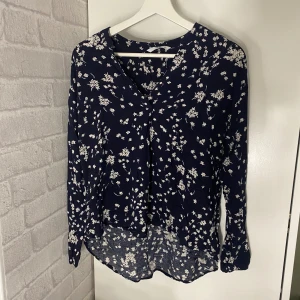 Blus - Marinblå blus med vita ”blommor” på. Som man ser så är den kortare nedtill där fram än baktill