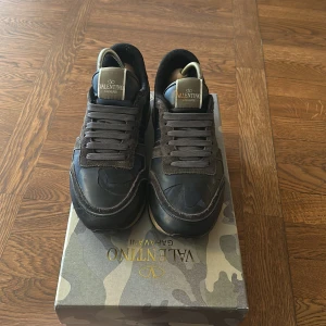 Valentino Rockrunners  - Snygga Valentino Garavani Rockrunner sneakers i mörka toner med svart och grå mocka, läderdetaljer och röd häl. De är använda men i bra skick 