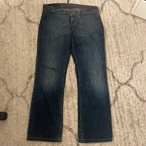 Mörkblå bootcut jeans från Levi's - Snygga mörkblå jeans från Levi's med klassisk bootcut passform. Jeansen har fem fickor, slitna detaljer vid benslut och kontrastsömmar. Materialet är robust denim som ger en cool vintagekänsla. Low waist 
