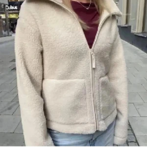 Beige teddyjacka från hm  - Mysig beige teddyjacka med hög krage och två stora fickor framtill. Jackan har en rak passform och stängs med dragkedja. Perfekt för dig som gillar en chill och varm look under höst och vinter. Materialet är fluffigt och ger en skön vibe.