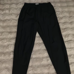 Svarta kostymbyxor från Kenzo - Svarta kostymbyxor från Kenzo i storlek S. Byxorna har en klassisk rak passform med elastisk midja och stilren design. Perfekta för dig som gillar en clean och snygg look. Materialet känns lätt och bekvämt mot huden.