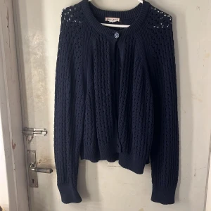 Mörkblå stickad kofta - Snygg mörkblå stickad kofta från Holly & Whyte med hålmönster och rund hals. Koftan har knappar framtill  och ribbade muddar vid ärmslut och nederkant. Perfekt för lager-på-lager och chill stil. Perfekt nu till höst&vinter