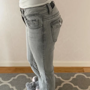 Grå jeans från Gina Tricot, storlek 32 - Snygga grå jeans från Gina Tricot i bootcut modell, fickor med lock och knapp. Modellen är lågmidjad.