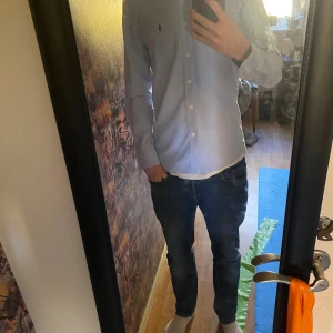 Ljusblå skjorta från Ralph Lauren - Snygg ljusblå skjorta från Ralph Lauren med klassisk button-down krage och vit knappstängning. Skjortan har lång ärm och en bröstficka med den ikoniska svarta Polo-loggan broderad. Perfekt för dig som gillar stilrena och tidlösa plagg. Han på bilden är 180 cm väger 68 kg. Super bra skick/nyskick