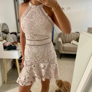 Ljusrosa spetsklänning med volang - Superfin ljusrosa kortklänning i spets med blommigt mönster och volang nertill. Hög halsringning och ärmlös modell med snygga detaljer i midjan. Perfekt för dig som vill sticka ut med en romantisk och trendig look.