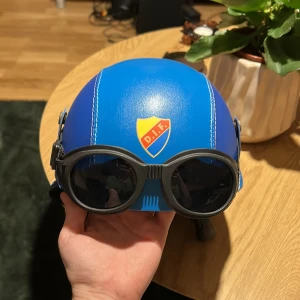 DIF Hjälm - Säljer en blå hjälm med DIF-märke framtill. Den har användbara svarta goggles och vita kontrastsömmar och öronlappar för extra stil. Perfekt för dig som vill sticka ut på match eller i backen så slipper man skidglasögon.