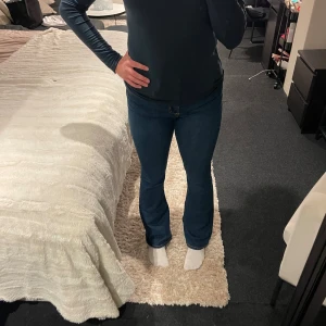 Blå bootcut jeans med hög midja - Snygga blå jeans med bootcut passform och hög midja. Klassisk femficksdesign och lätt stretch i materialet för skön komfort. Perfekta för dig som gillar en retro vibe och vill ha jeans som sitter tajt upptill och släpper vid benen.