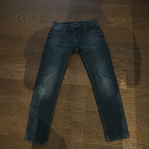 Mörkblå jeans från Lufian - Snygga mörkblå jeans från Lufian med klassisk femficksdesign och L.E.N broderat på myntfickan. Jeansen har en rak passform och subtila slitningar för en cool look. Perfekt för dig som gillar stilrena och tidlösa jeans.