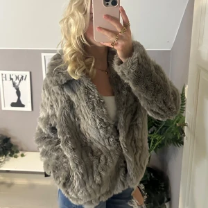 Grå pälsjacka från Vila - Säljer en fluffig och snygg grå pälsjacka från Vila med bred krage och dold knäppning framtill. Jackan har en loose passform och är helfodrad för extra komfort. Perfekt för dig som vill ha en cool och trendig look under höst och vinter.