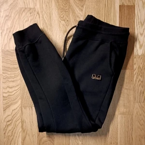 Svarta mjukisbyxor från 19v69 Italia  (dam - Svarta mjukisbyxor från 1969 Italia med broderad logga i guld på vänster ben. Byxorna har snörning i midjan och är tillverkade i mjukt, fleeceliknande material. Perfekta för chill eller träning, med normal passform och bekväma muddar vid bensluten. Från versaces senaste märke ordinarie pris köpt med rabbat för 1500kr storlek  storlek L  använd ett väldigt fåtal ggr då hon är som mig gilla håller plaggen rent o fräscha 