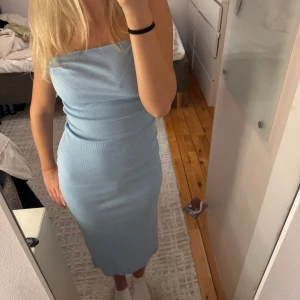 Ljusblå ribbad långklänning - Säljer en ljusblå, ribbad långklänning med slits där bak. Klänningen är axelbandslös och har en tight passform som framhäver figuren.