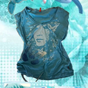 Blå topp med ansiktsprint och fjärilar - Säljer en blå topp med ett stort tryck av ett ansikte, fjärilar och stjärnor på framsidan. Toppen har rund halsringning, ärmlös design och snörning längst ner. Perfekt för dig som gillar unika motiv och coola detaljer.