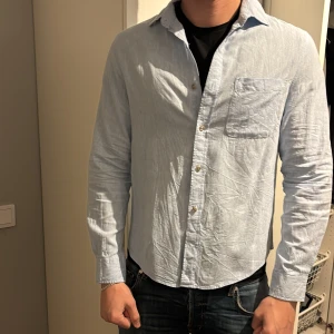 Ljusblå bomullsskjorta med ficka - Ljusblå skjorta i bomull med klassisk krage och bröstficka. Skjortan har knappar framtill och långa ärmar med manschett. Perfekt för en avslappnad men ändå stilren look. Storlek s men passar m lite bättre. Köpte den men aldrig använt då den var för lång på mig