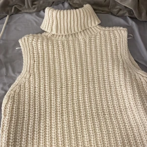 Stickad beige väst med polokrage H&M - Säljer en chunky stickad väst från H&M i beige med bred polokrage. Västen har grov ribbad struktur och är ärmlös, perfekt att layera över en skjorta eller långärmad. Mjuk och cozy vibe, passar dig som gillar clean och enkel stil.