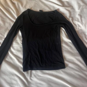Svart långärmad topp med rund hals - En enkel och stilren svart långärmad topp med rundad halsringning. Perfekt att matcha med jeans eller kjol för en clean look. Tunn och mjuk i materialet, sitter snyggt och följsamt på kroppen.