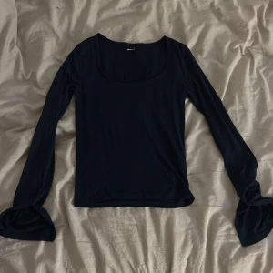 Mörkblå långärmad topp Gina Tricot - Snygg mörkblå långärmad topp från Gina Tricot med rundad, djup halsringning. Tunn och mjuk i materialet, perfekt för layering. Ärmarna är långa och har en lätt slits vid mudden för extra detalj. Enkel och stilren design som funkar till många looks.