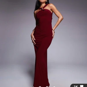 Vinröd långklänning med öppen rygg - Supersnygg vinröd långklänning med asymmetriska axelband och en cool öppen rygg. Klänningen har en tight passform och är tillverkad i ett mjukt, stretchigt material som sitter perfekt. Perfekt för dig som vill sticka ut med en elegant och modern look.