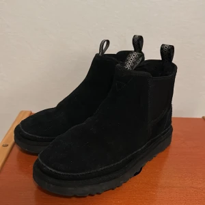 Svarta UGG boots i mocka - Säljer ett par svarta boots från UGG i mjuk mocka med fluffigt foder. Skorna har elastiska paneler på sidorna och grov sula för extra komfort. Ny pris cirka 2000kr, perfekt till kommande vintern!