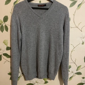 Grå v-ringad 100% Kashmir tröja  - Säljer en stilren grå stickad tröja med v-ringad hals. Tröjan har långärmade och ribbade muddar vid ärmslut och nederkant. Perfekt för dig som gillar enkel och klassisk look. 100% Kashmir 